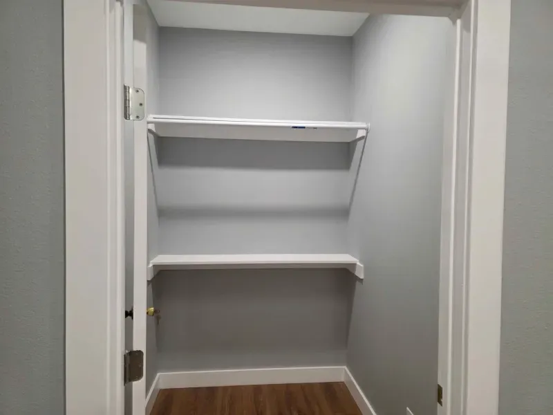 Empty gray closet with two white shelves and a wooden floor