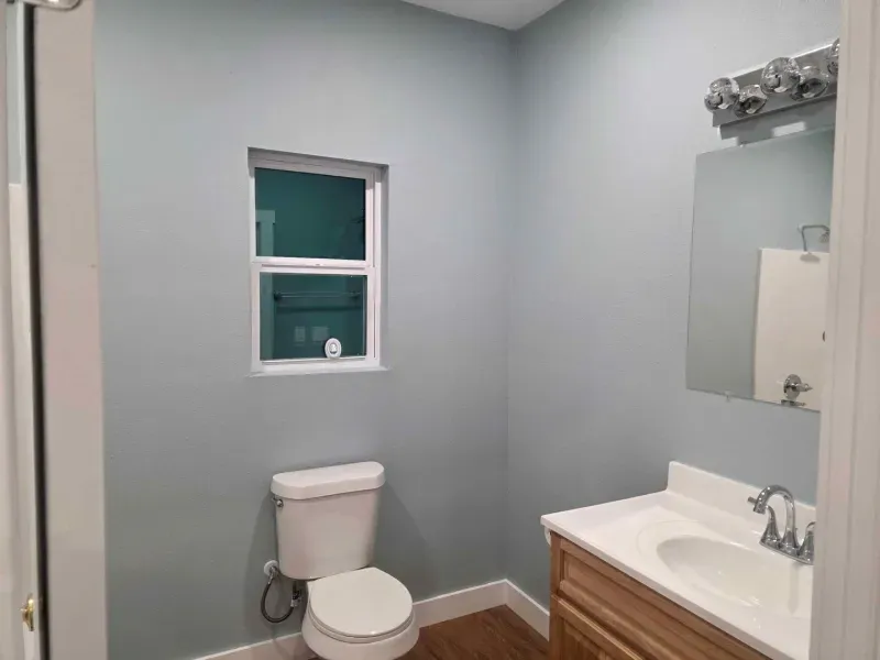 Small bathroom with gray walls, a toilet under a window, and a white vanity with mirror.