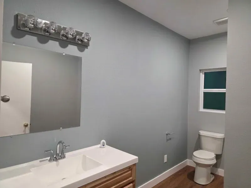 Gray bathroom with white vanity, mirror, and toilet near a small window.