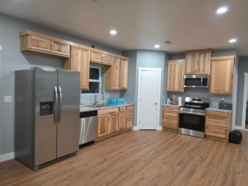 Modern kitchen with stainless steel appliances, light wood cabinets, gray walls, and wood-look flooring