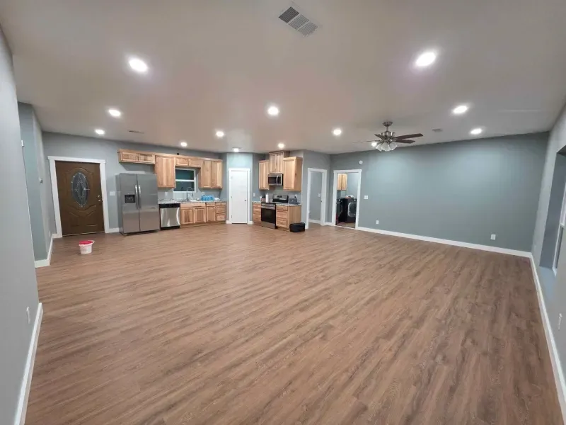 Empty open-plan living room with wood floors, gray walls, recessed lights, and a kitchen area
