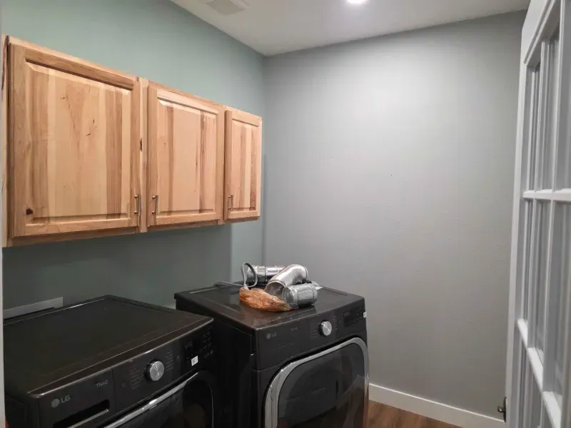 Laundry room with wood cabinets, black washer and dryer, and a small gray windowed wall.