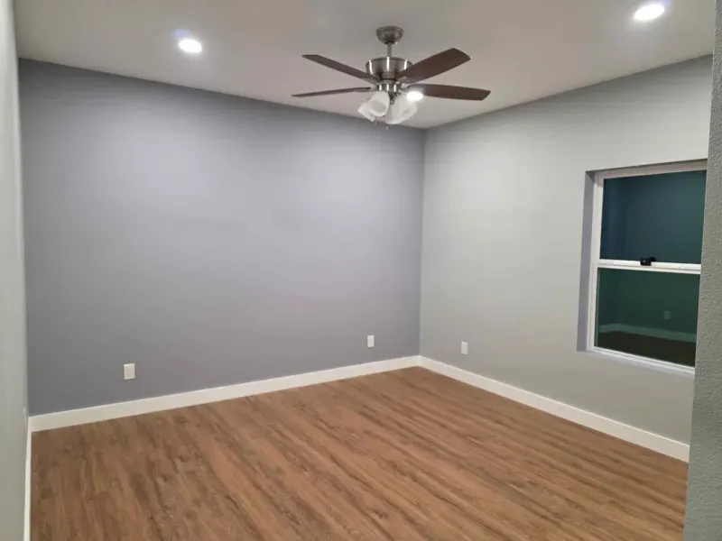 Empty room with wood floors, light gray walls, ceiling fan, recessed lights, and one window.