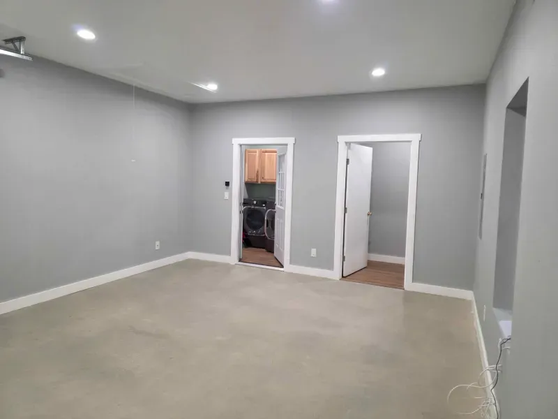 Empty gray room with beige carpet, recessed lights, and two open doorways.