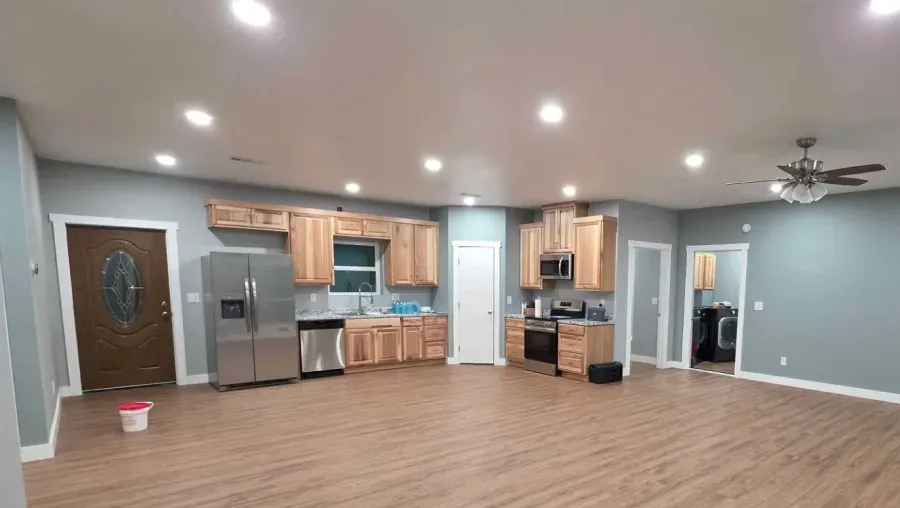 Open-concept living room and kitchen with wood floors, stainless appliances, gray walls, and ceiling lights