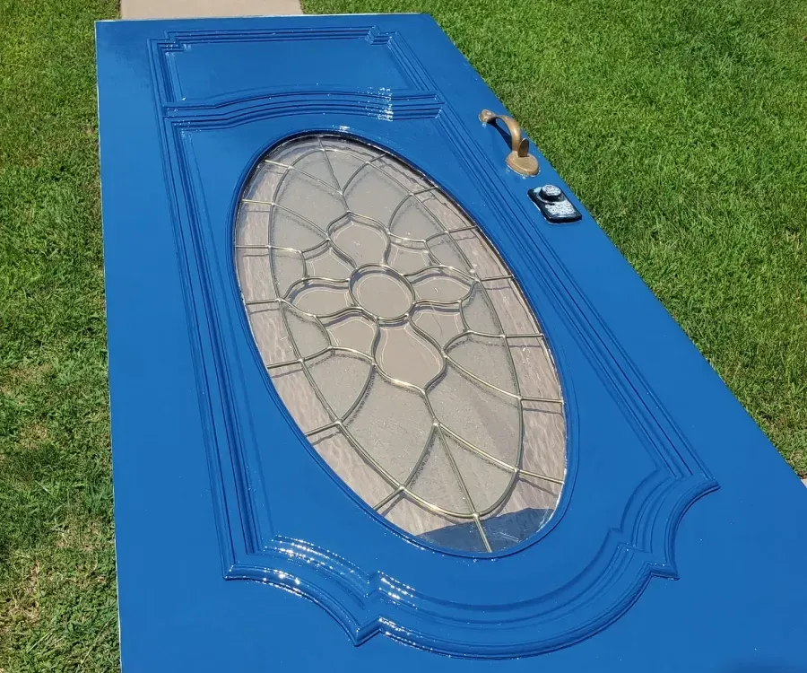Blue front door with oval leaded-glass window and brass hardware, lying on grass.