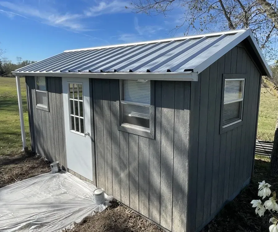 Small gray shed with a metal roof in a grassy yard under a blue sky