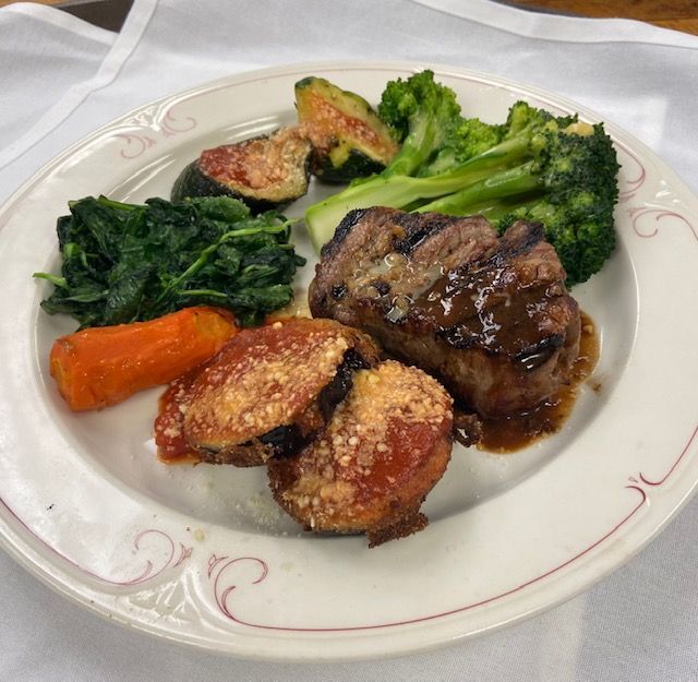 Plated meal with steak, broccoli, carrots, and greens on a white plate