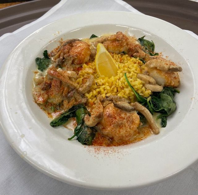 Plated seafood risotto with yellow rice, greens, mushrooms, and a lemon wedge