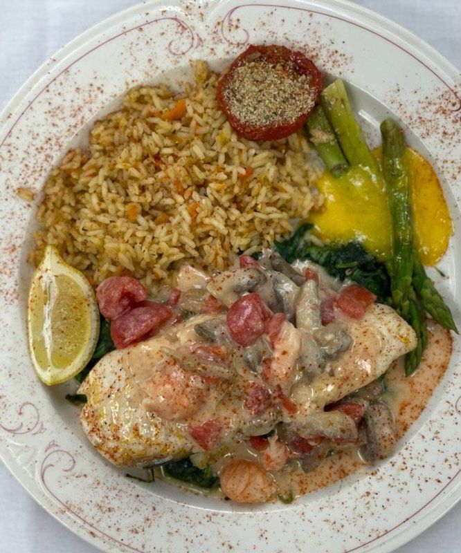 Plated meal with rice, chicken, lemon wedge, asparagus, and sauce on a white plate