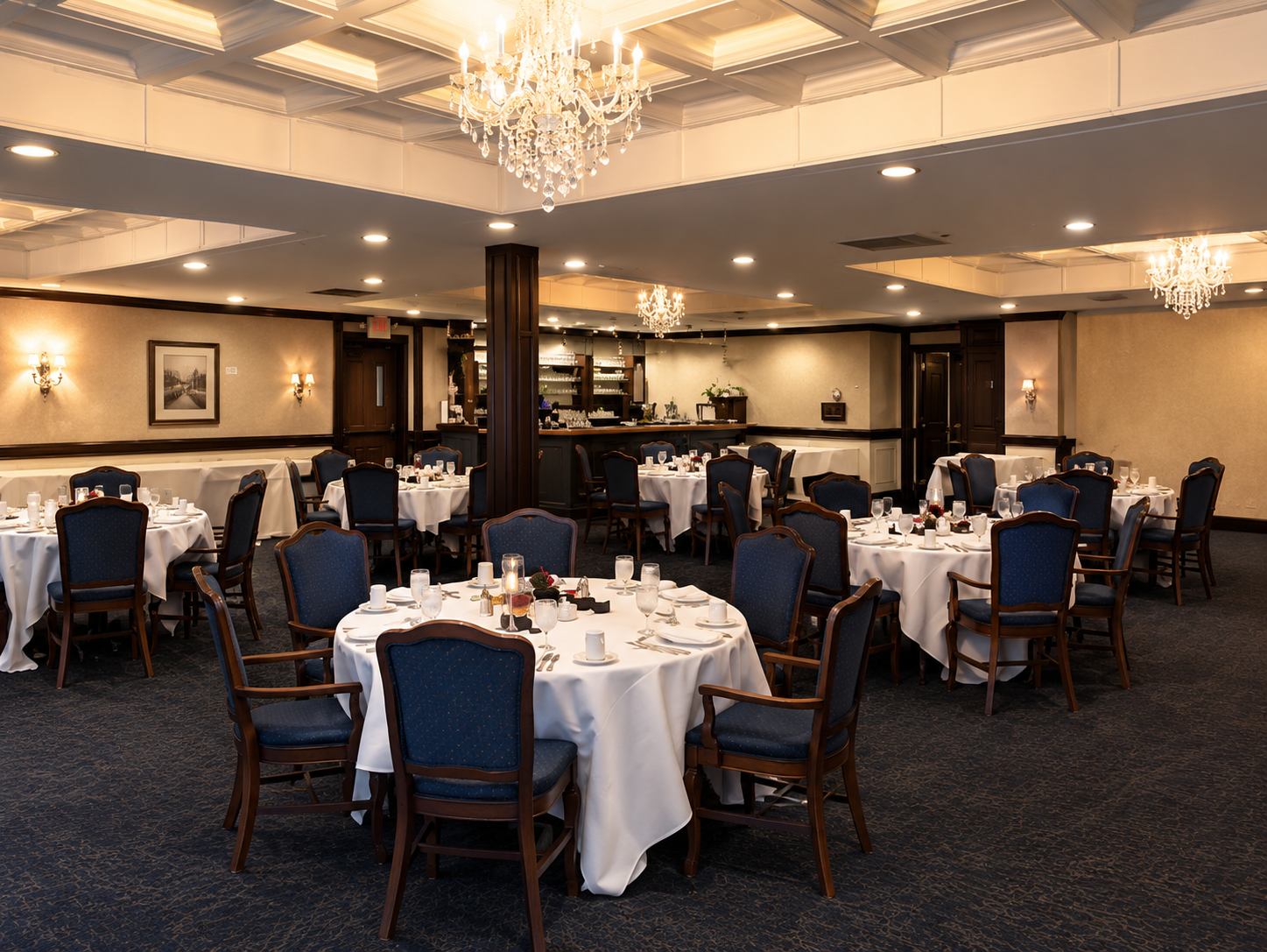 Elegant banquet hall with round tables, white tablecloths, blue chairs, and chandeliers.