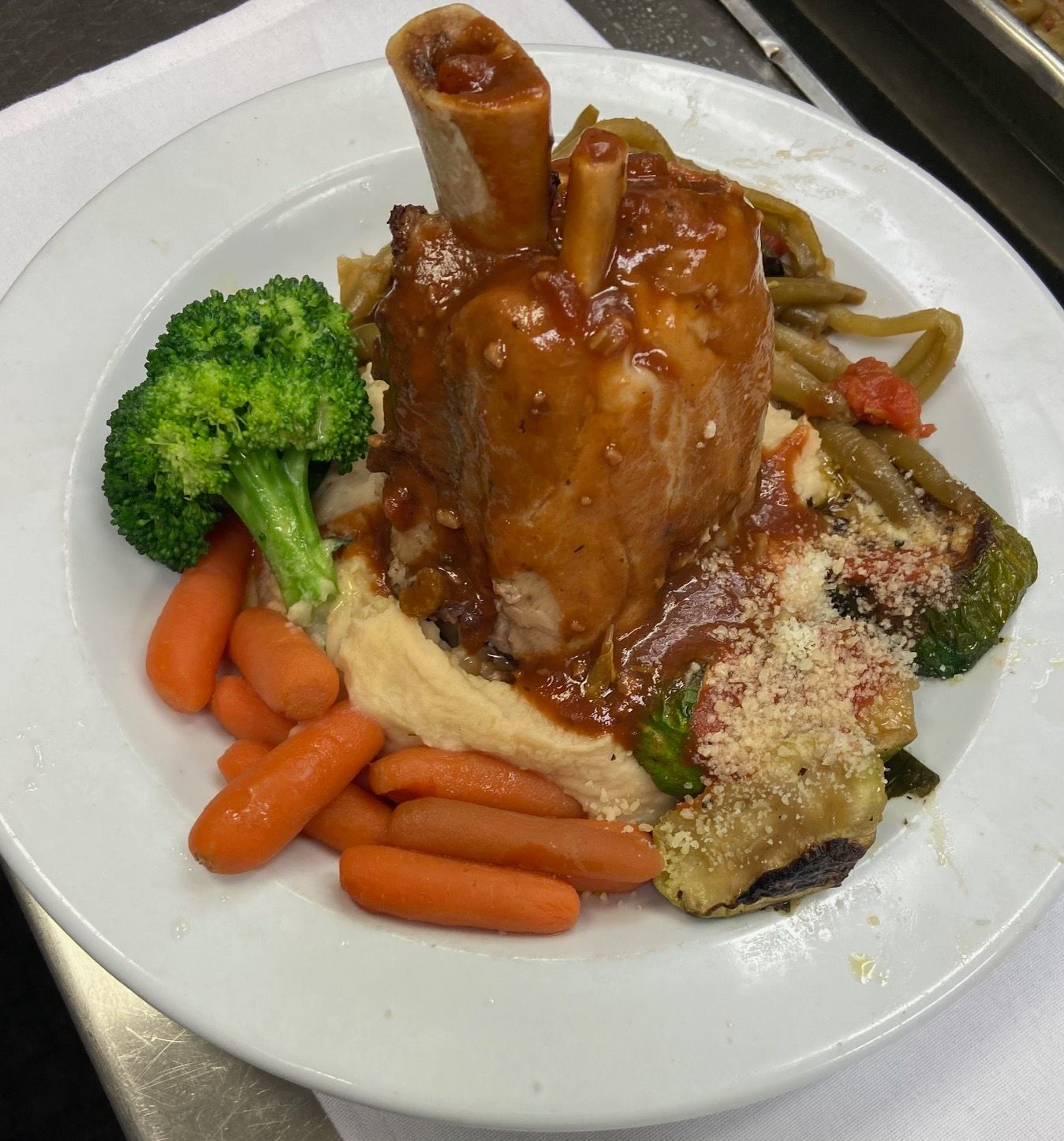 Roasted meat with gravy, broccoli, carrots, and mashed potatoes on a white plate