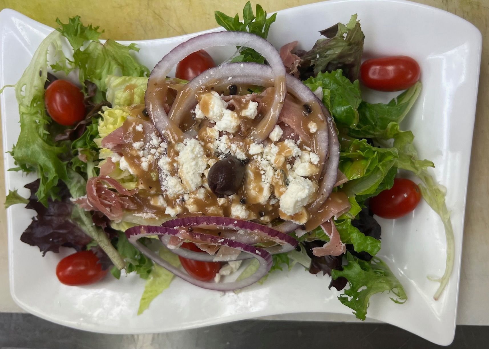 Salad with mixed greens, cherry tomatoes, red onion rings, feta, and balsamic glaze on a white plate