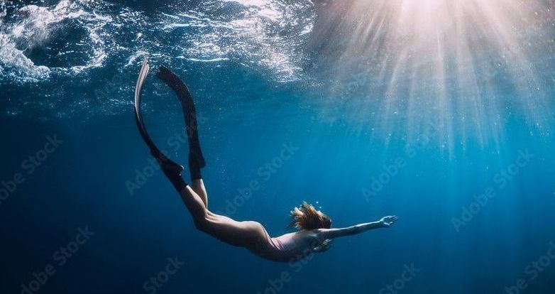 A woman is swimming underwater in the ocean.