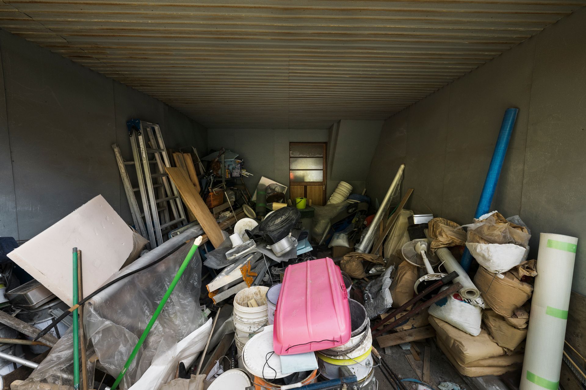 A cramped, cluttered storage space filled with various household items, construction materials, and loose debris.