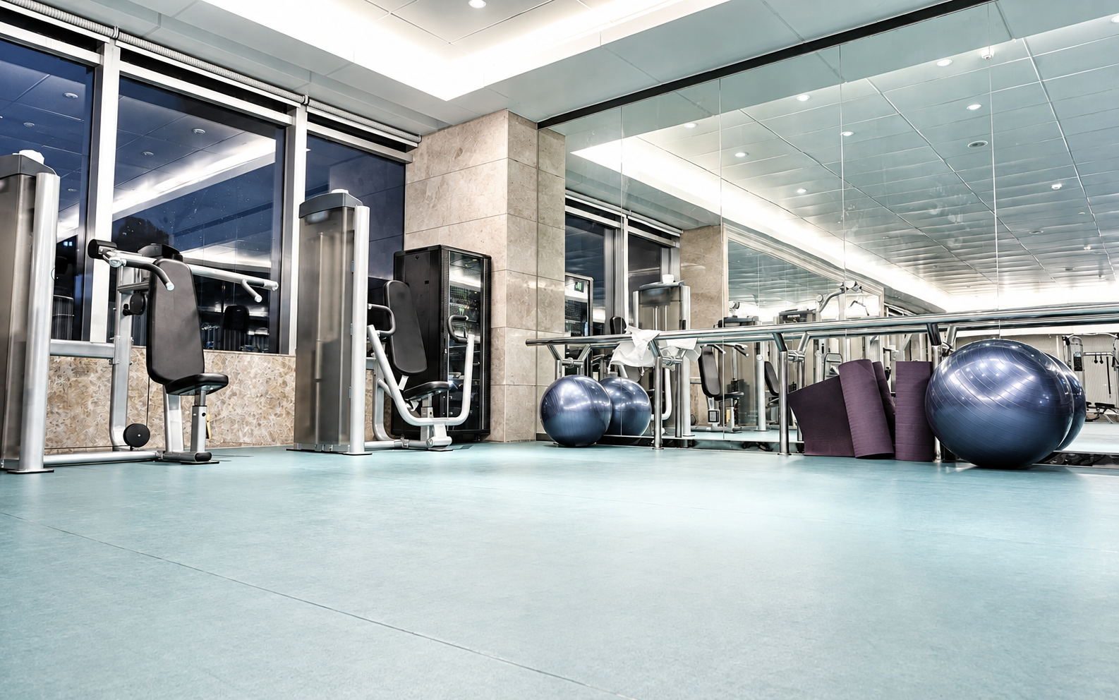 Modern gym interior with exercise machines, large mirrors, stability balls, and blue flooring