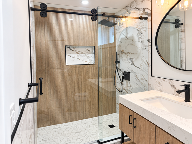 Modern bathroom with glass shower, wood vanity, marble accents, and round mirror