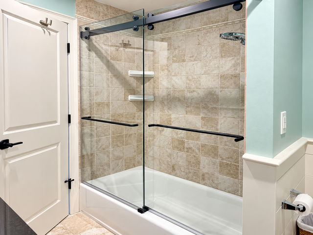 Glass-enclosed bathtub shower with beige tile and white door in a bathroom