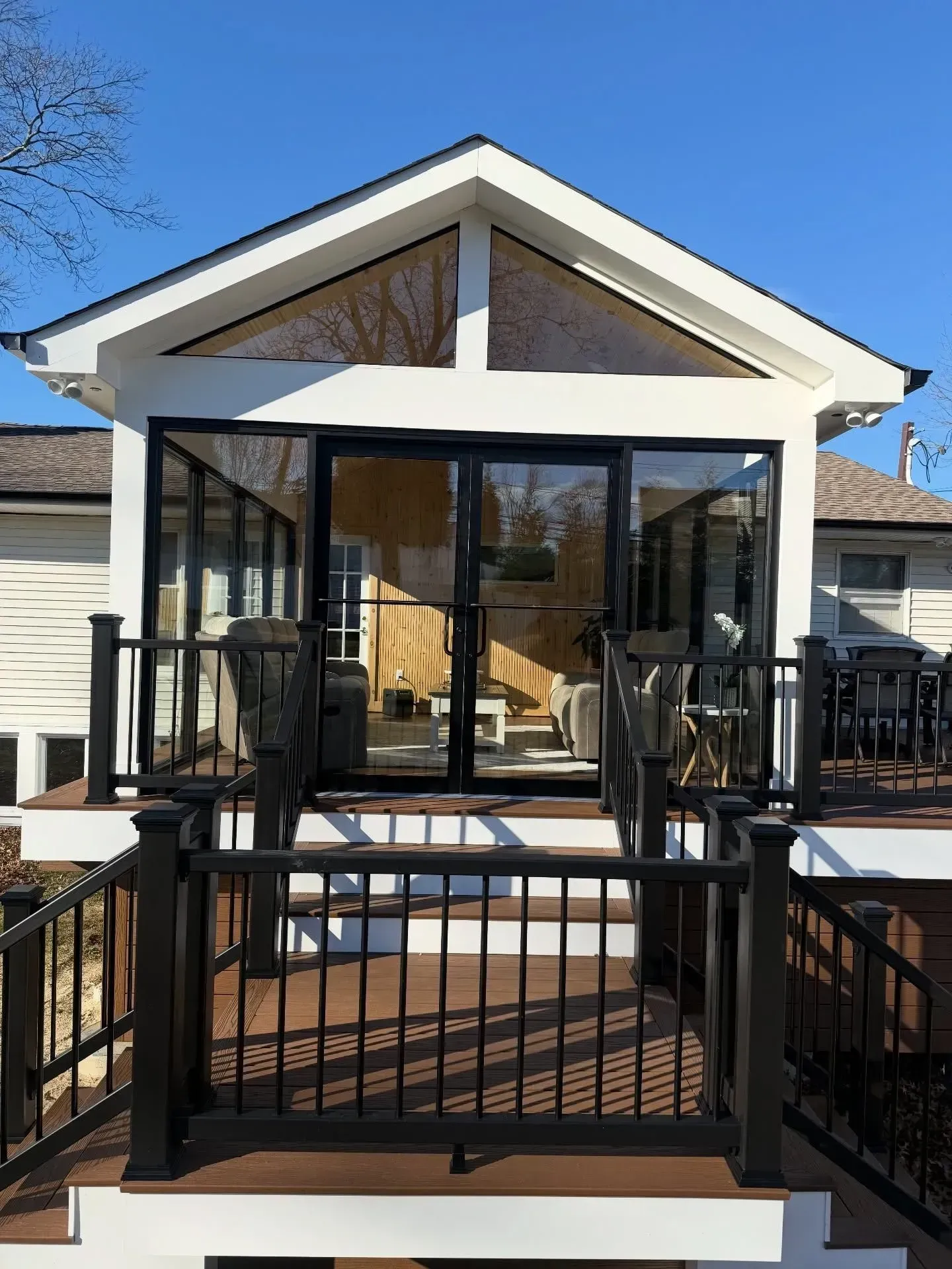 Front porch with black railing and screened entry on a small house under a blue sky