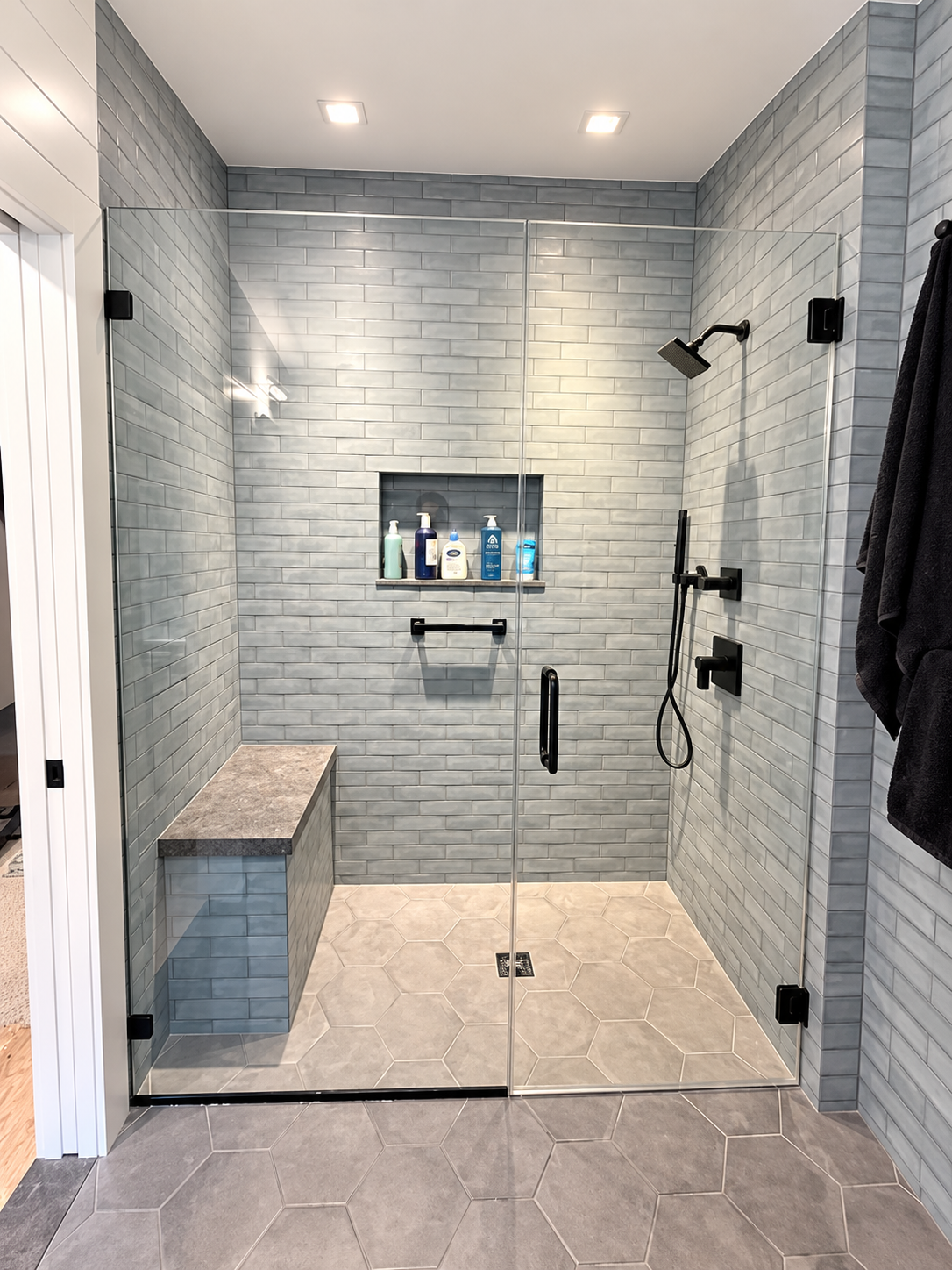 Modern tiled walk-in shower with bench, glass doors, and black fixtures