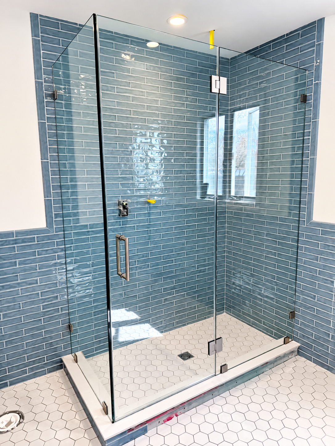 Glass-enclosed shower with blue tile walls and white hexagon floor tile in a bathroom