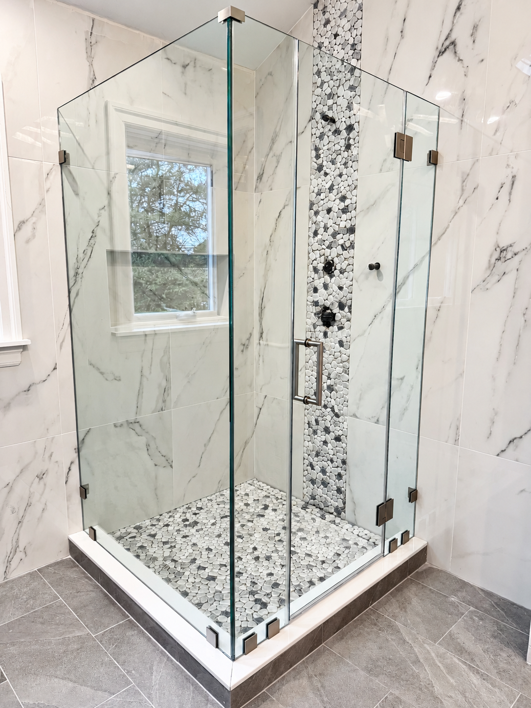 Glass shower enclosure with marble walls and pebble floor in a modern bathroom