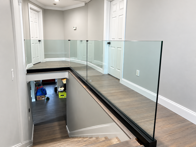 Interior hallway with glass railing overlooking a lower stairwell, gray walls, and wood floors