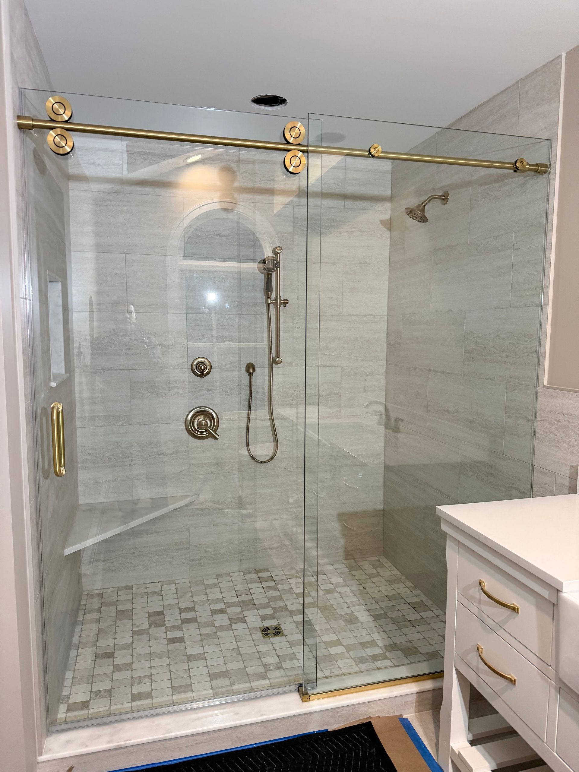 Glass walk-in shower with marble tile, brass hardware, and white vanity in a bright bathroom