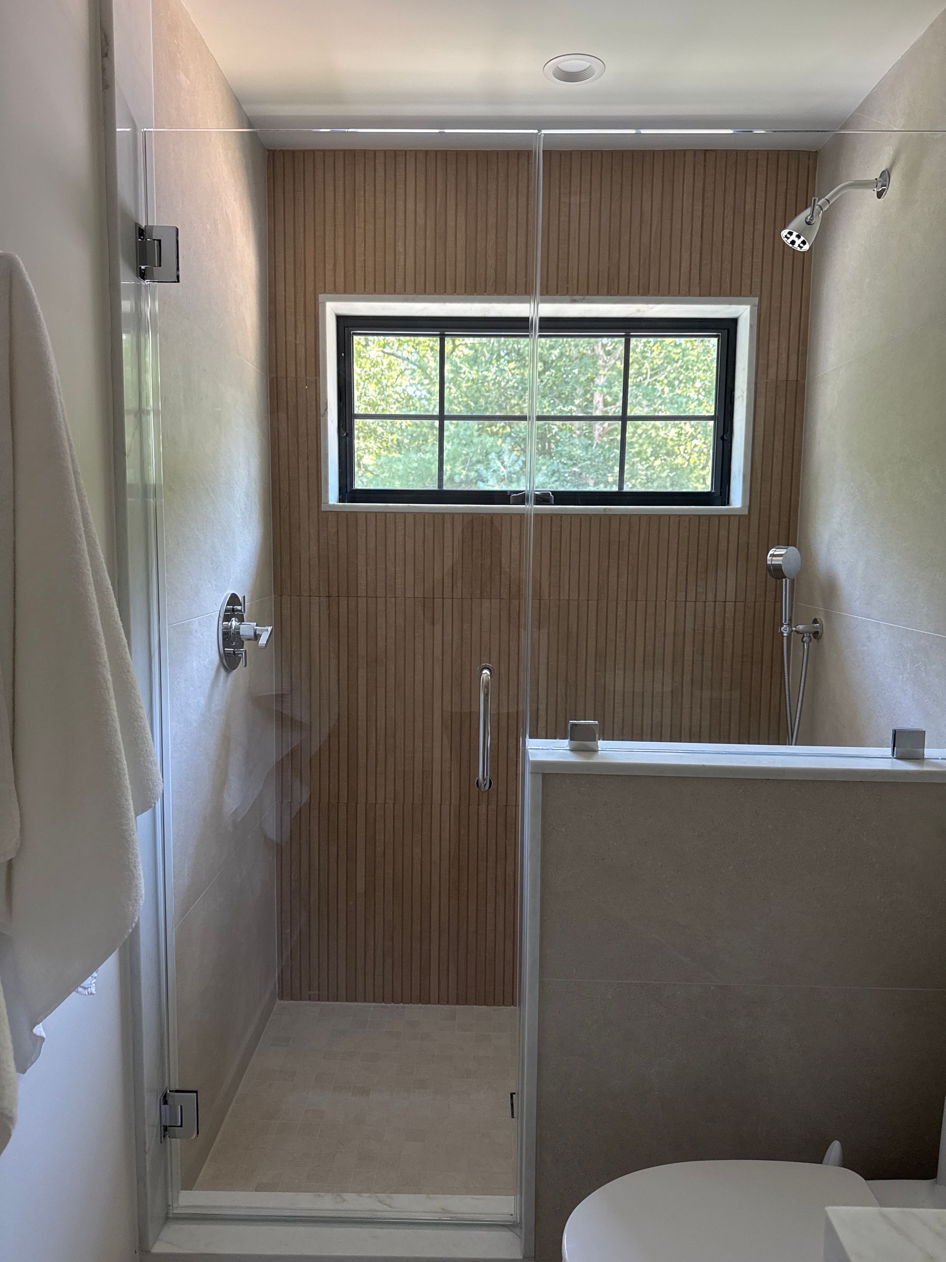 Bathroom with walk-in shower, wood-paneled back wall, and small window.