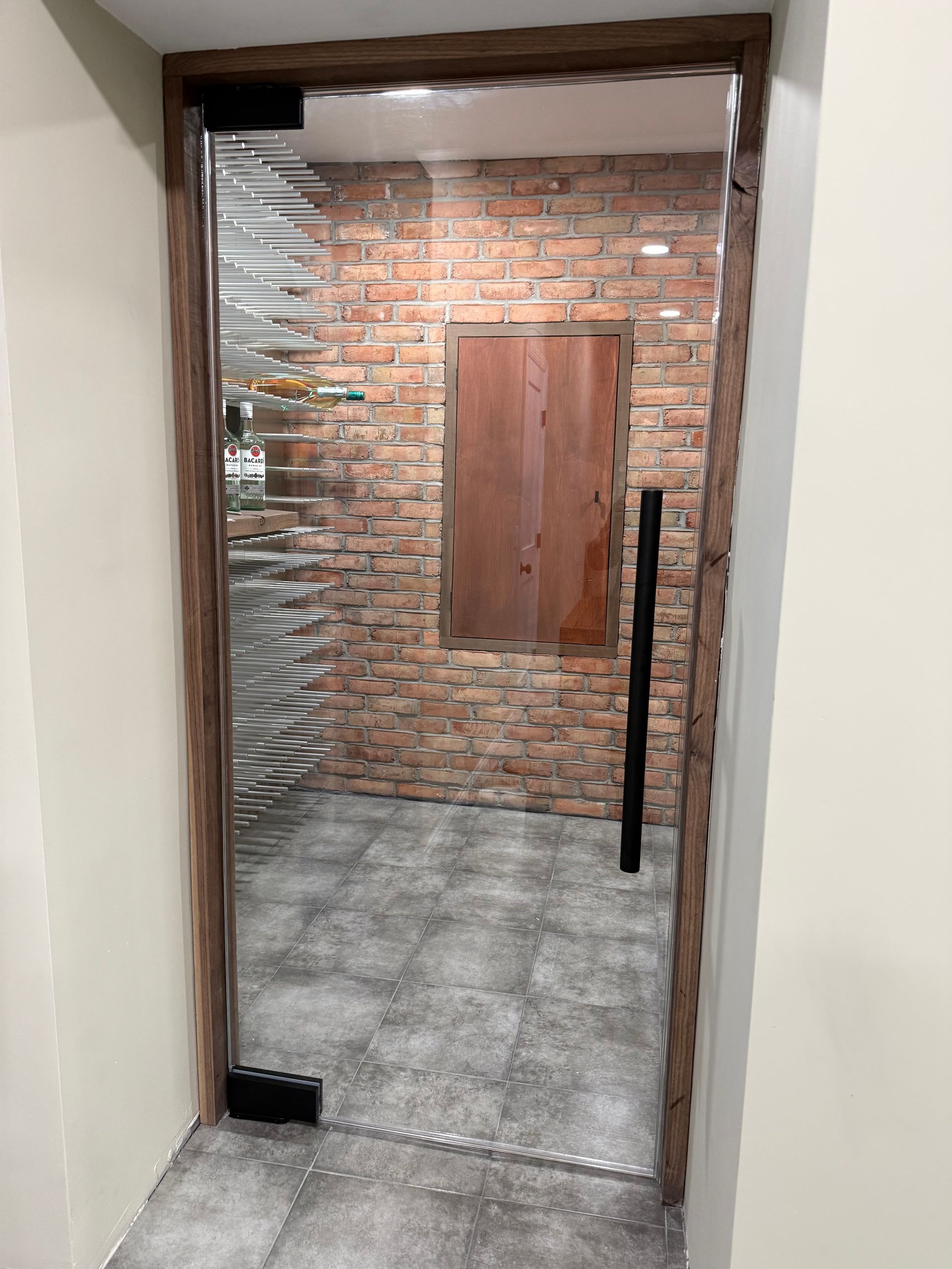 Doorway into a brick-walled room with a metal-framed glass door and gray tile floor