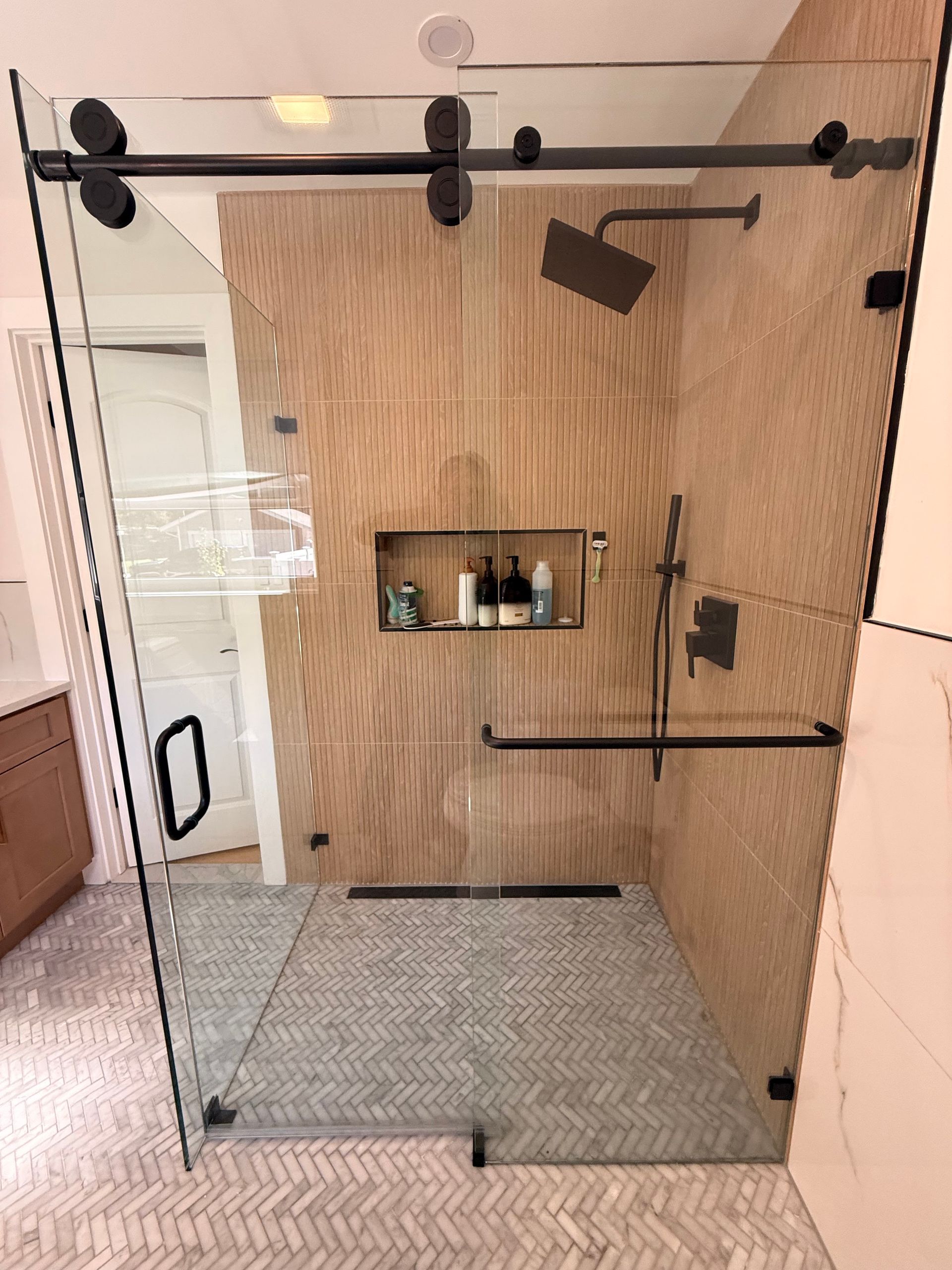 Glass shower enclosure with wood-look tile walls, black fixtures, and a shower niche in a bathroom