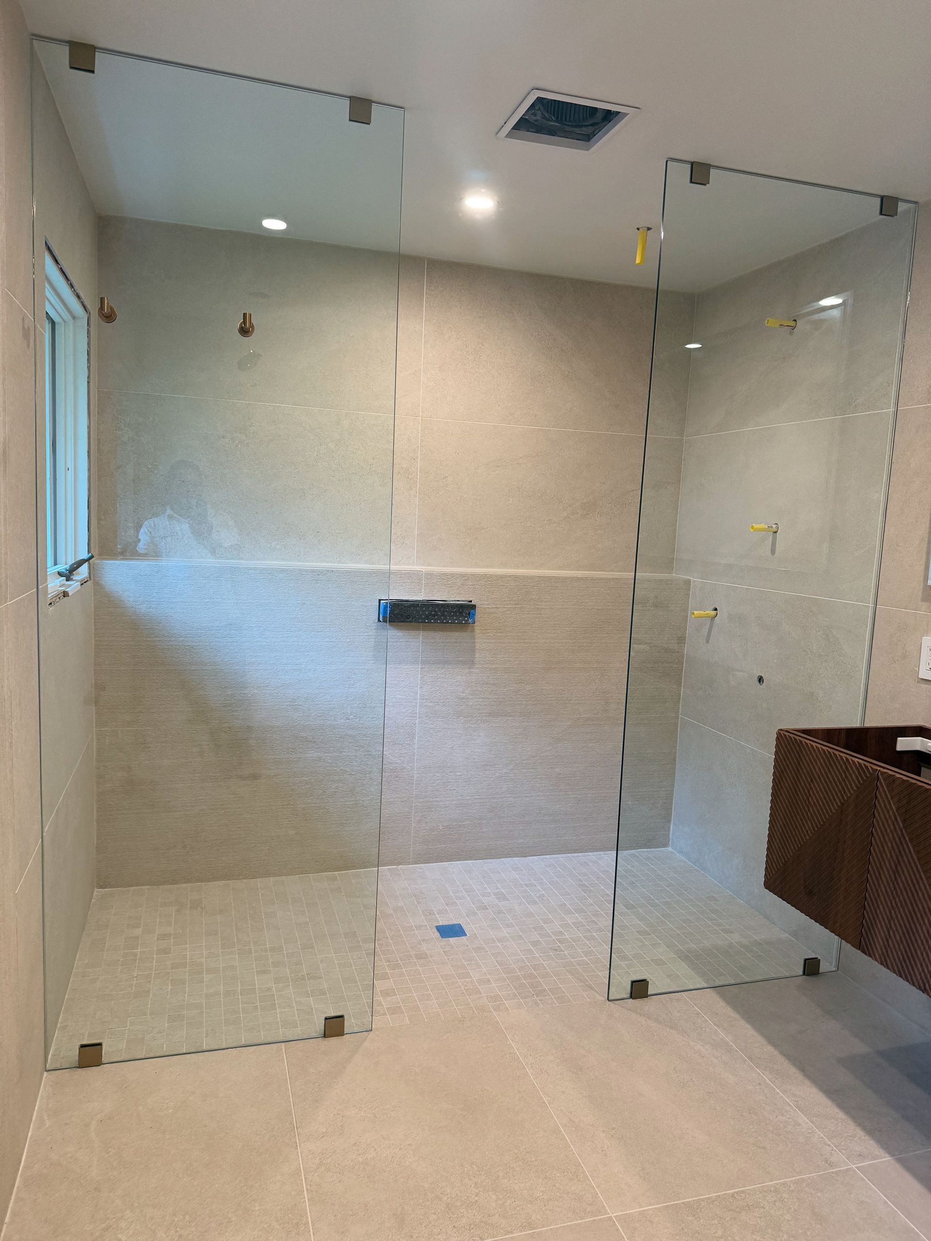 Modern bathroom shower with clear glass panels, beige tile walls, recessed lights, and a wicker basket.