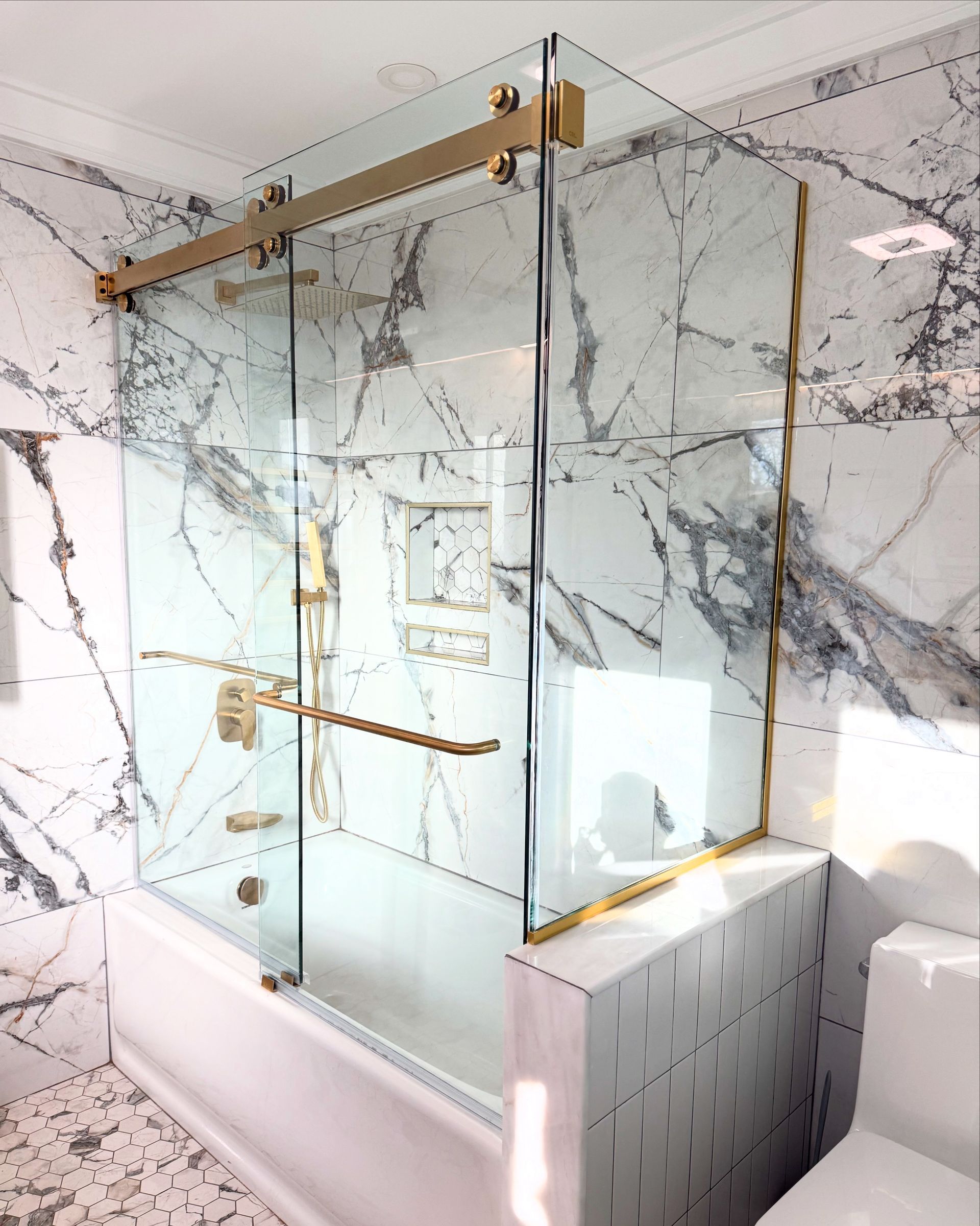Modern bathroom with marble walls, glass shower enclosure, and brass hardware