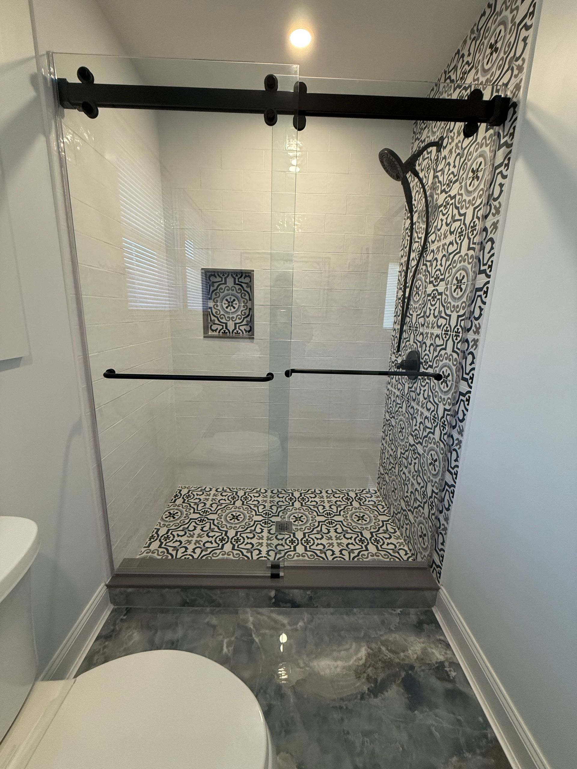 Bathroom with walk-in shower, glass door, black fixtures, and tiled floor.