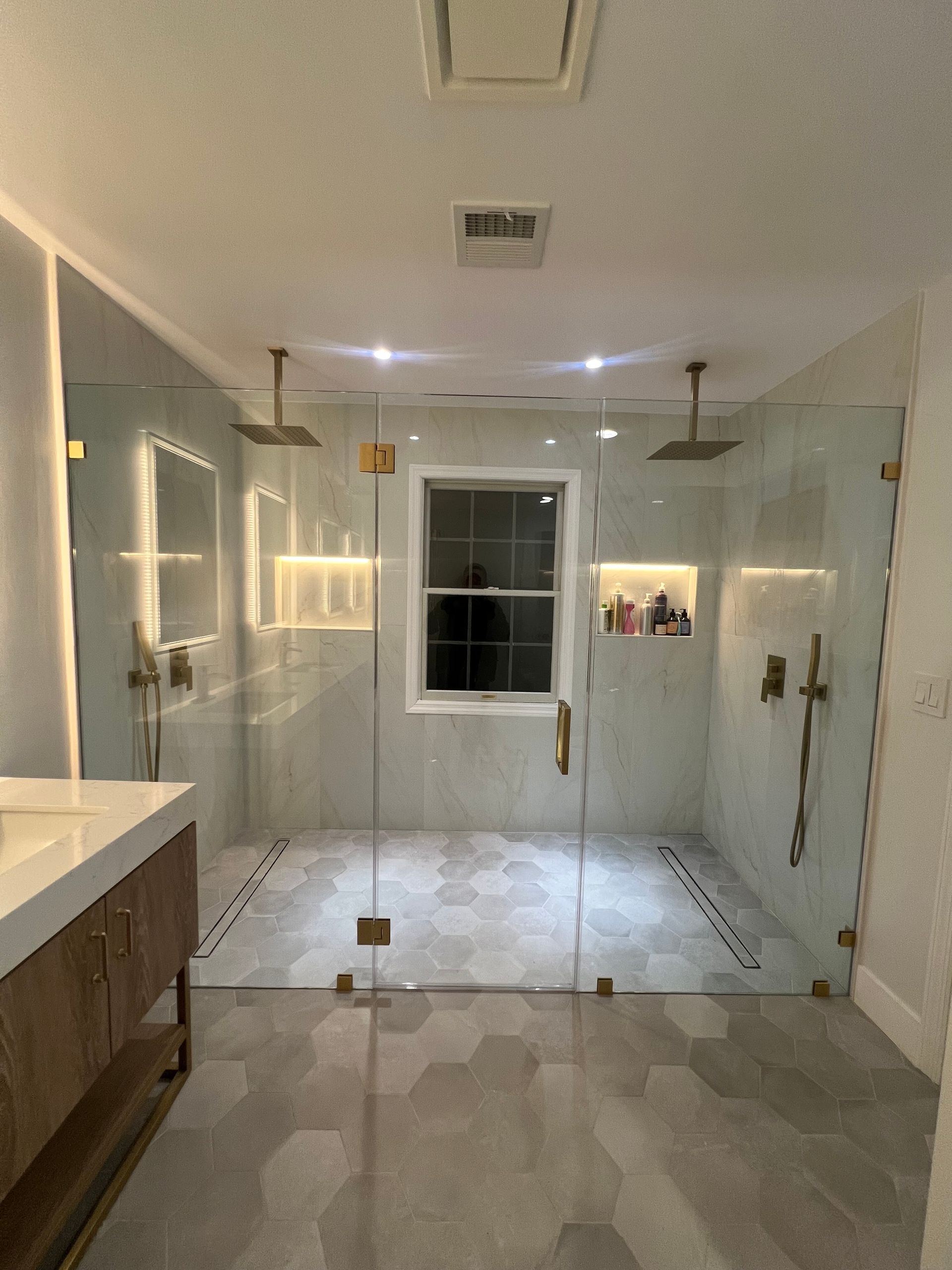 Modern bathroom with glass walk-in shower, double vanity, tiled floor, and window at the back