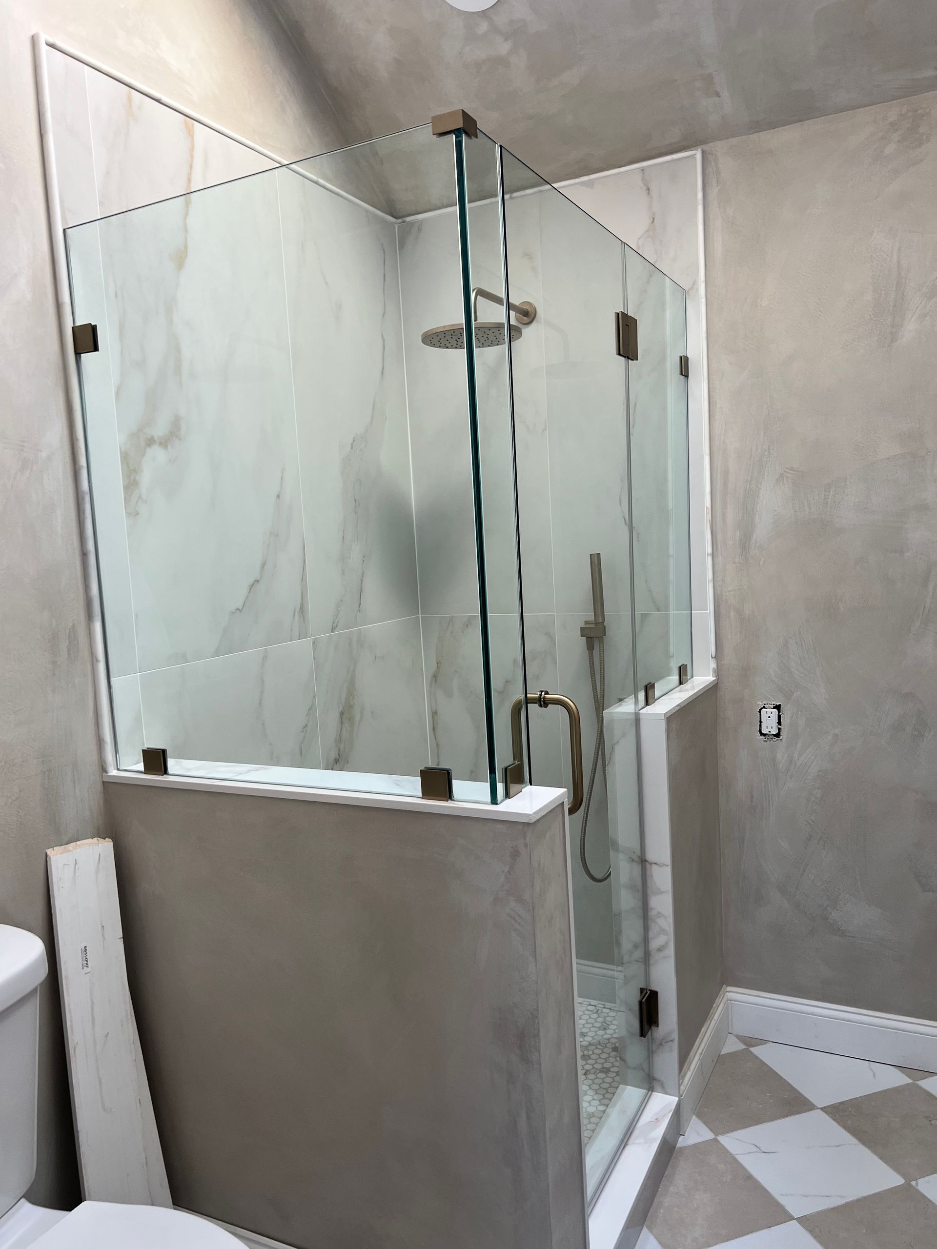 Glass walk-in shower with frosted doors and chrome fixtures in a gray-tiled bathroom
