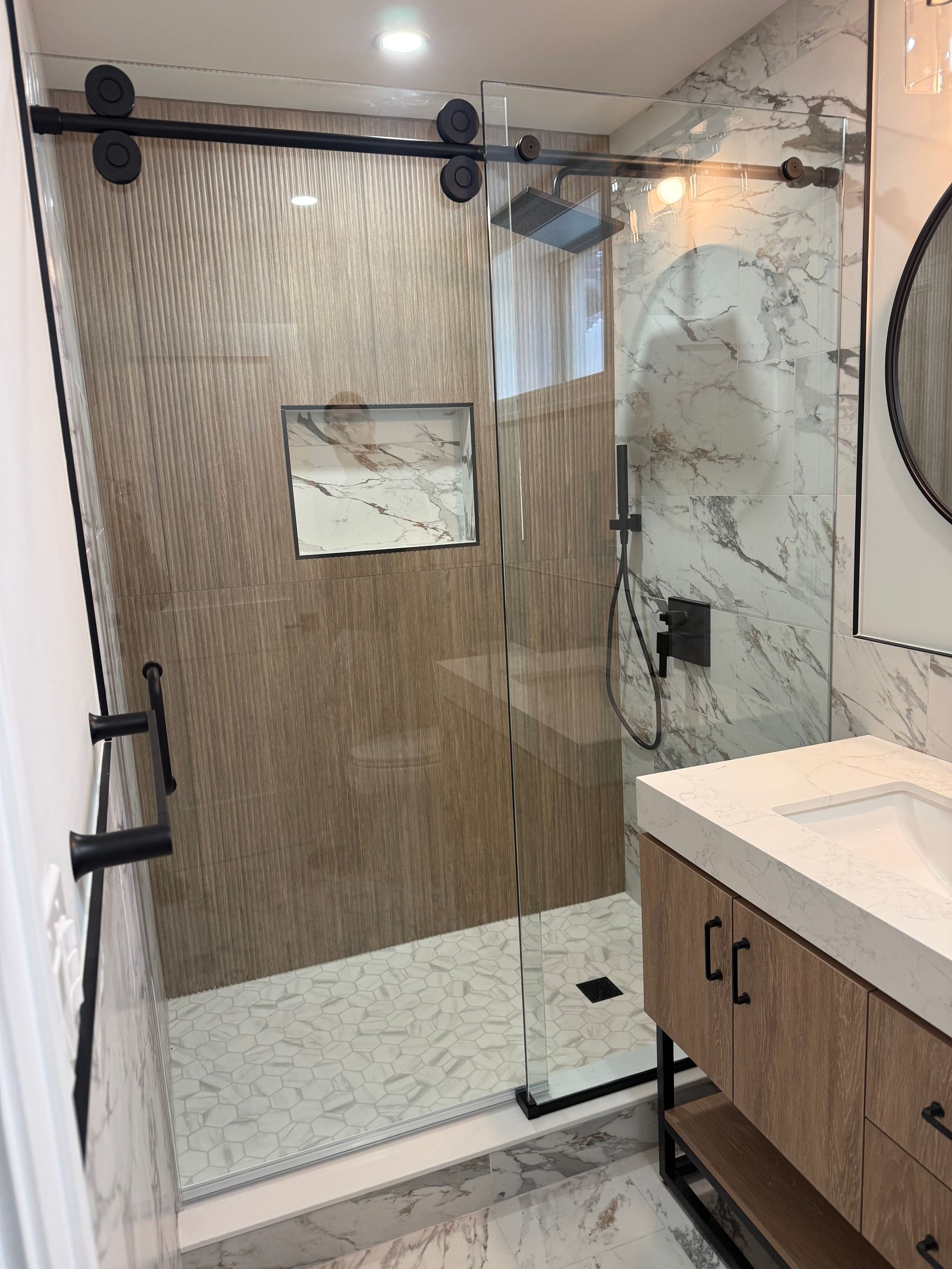 Modern bathroom with glass walk-in shower, beige tiled wall, and wood vanity with white countertop.