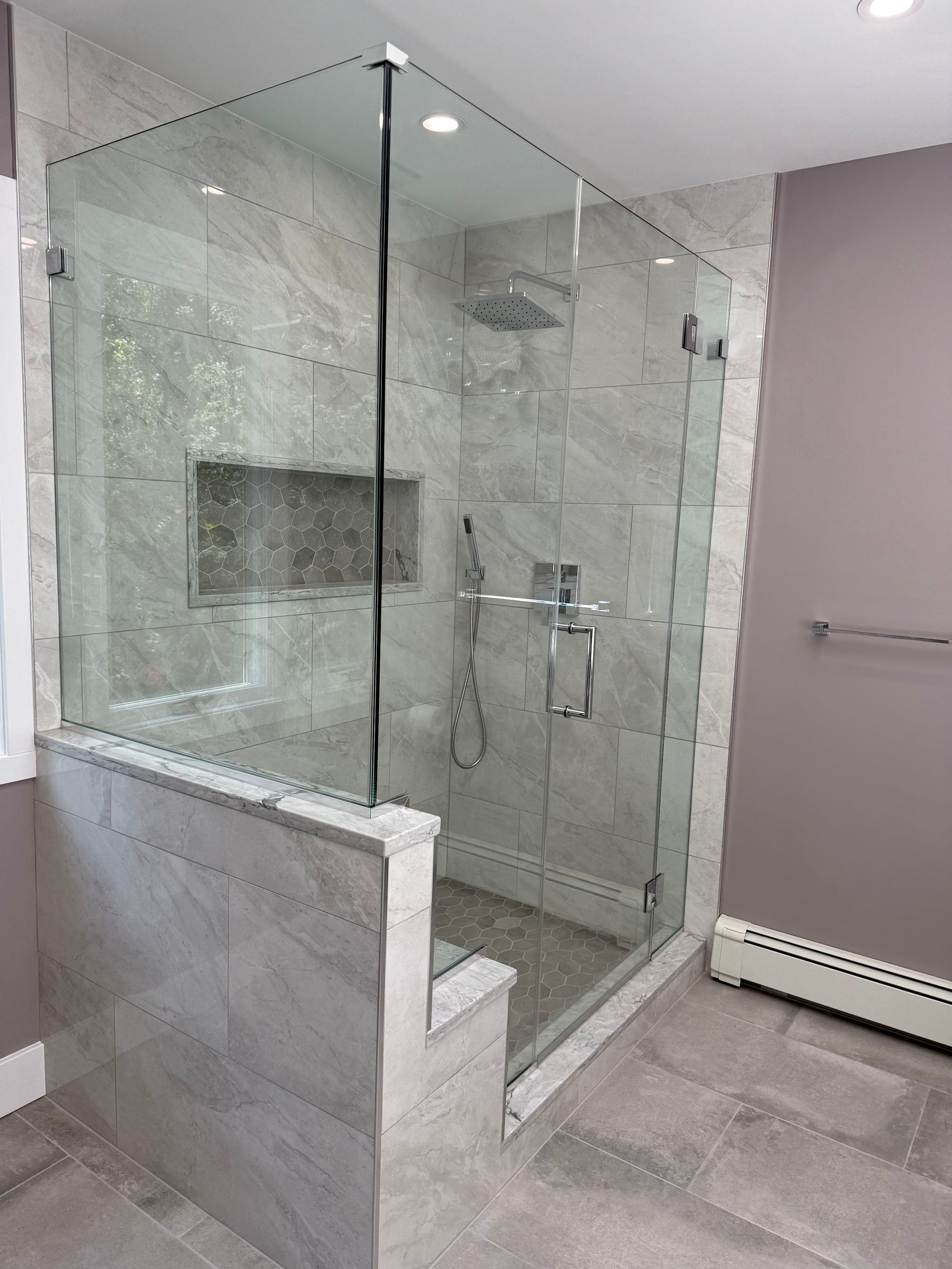 Modern glass-enclosed walk-in shower with gray tile in a tiled bathroom