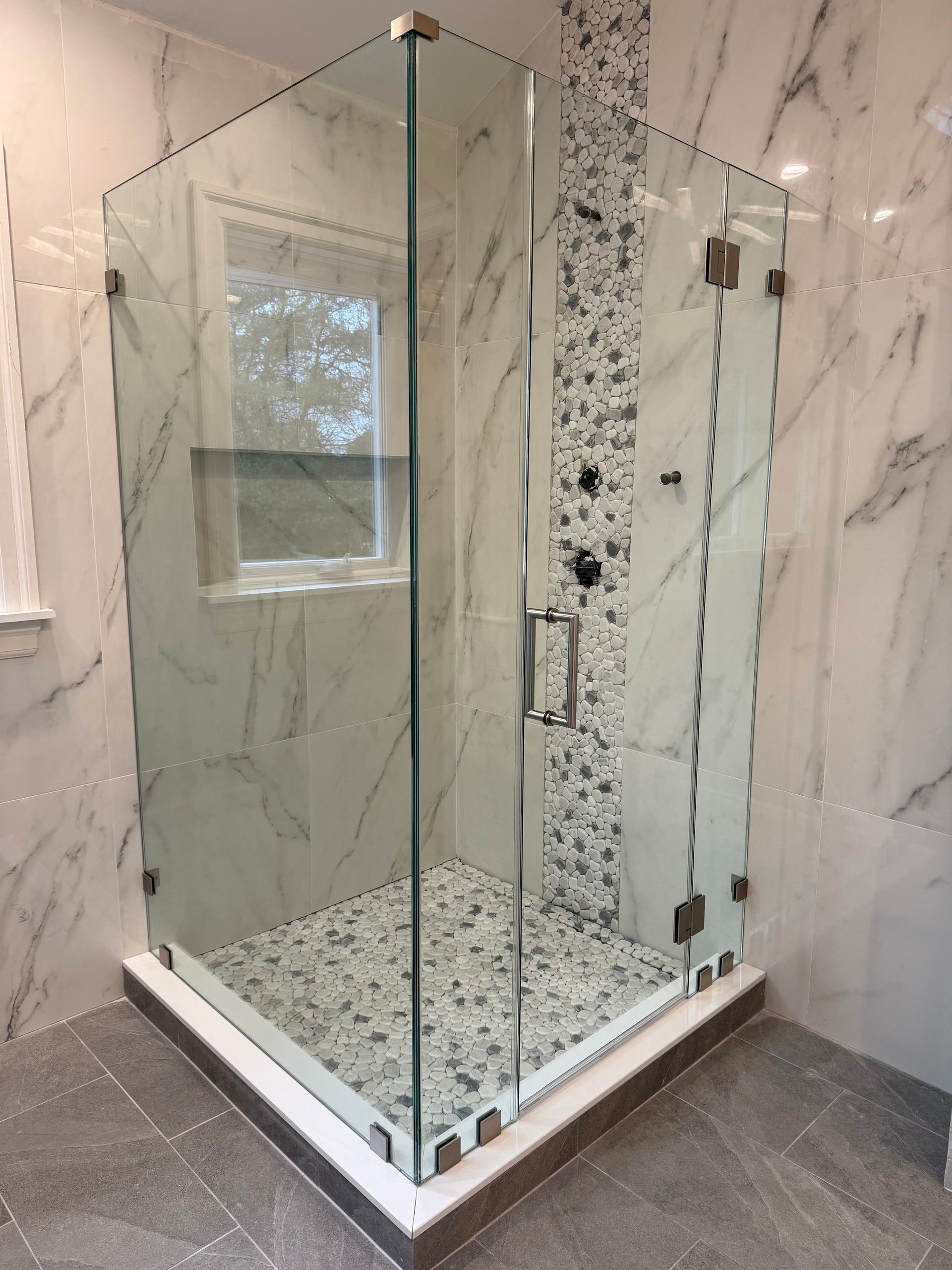 Glass shower enclosure with white marble walls and pebble floor in a modern bathroom