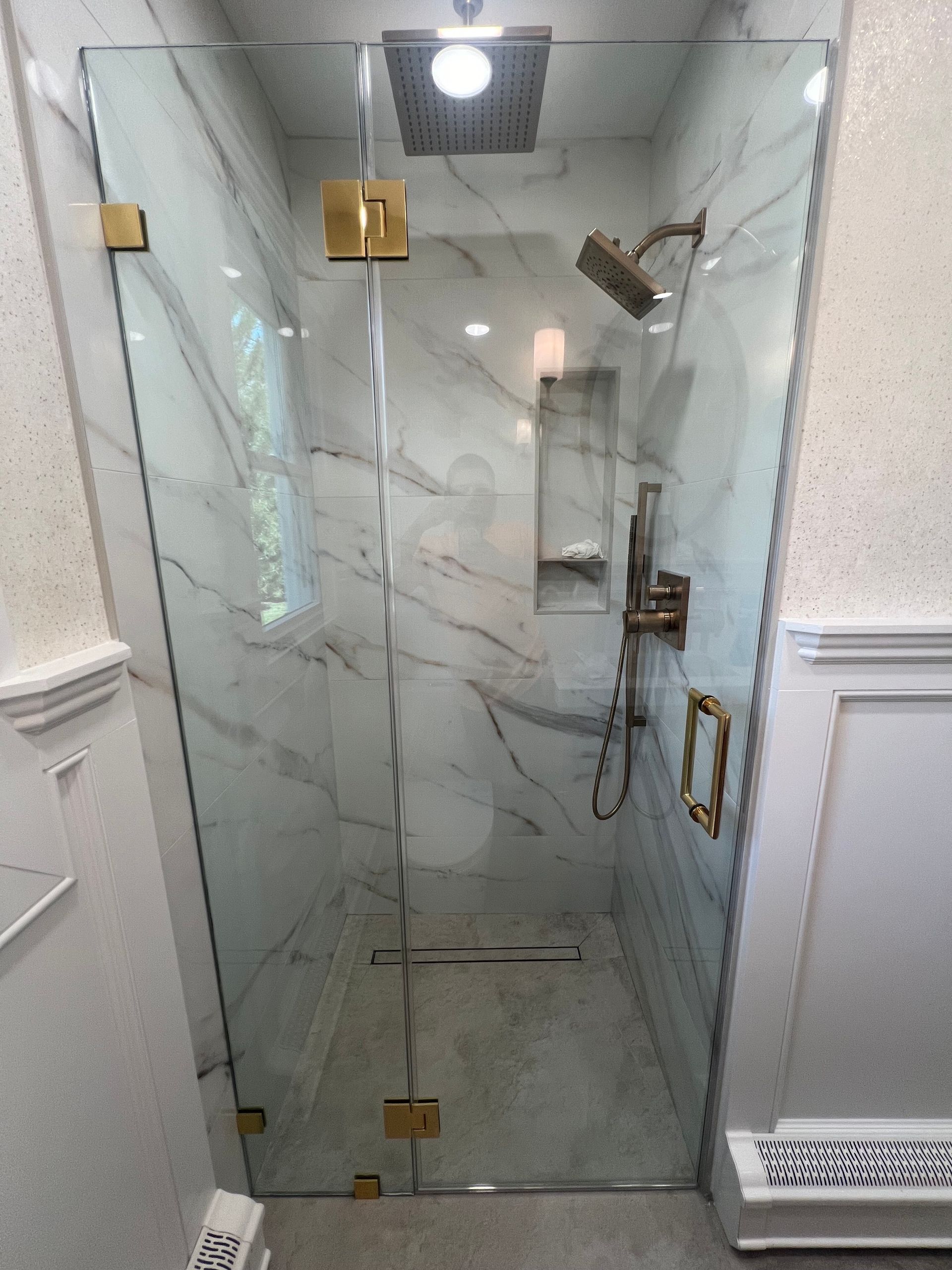 Glass shower stall with gold hardware and marble-pattern walls in a bathroom
