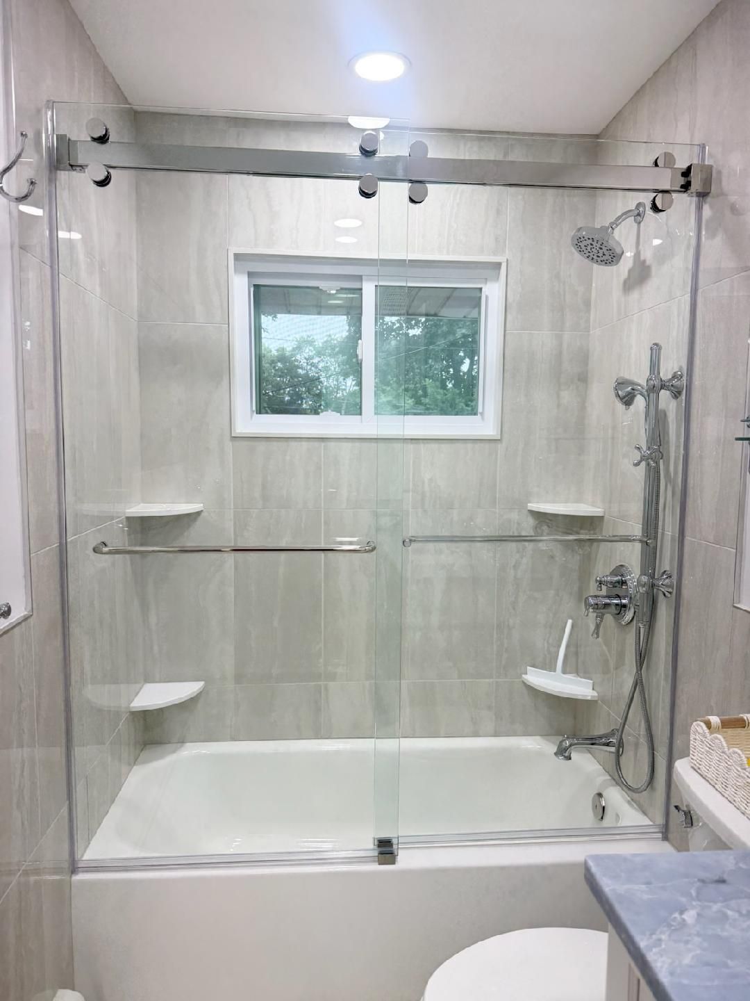 Accessible bathroom with grab bars, shower bench, and tub beneath a window