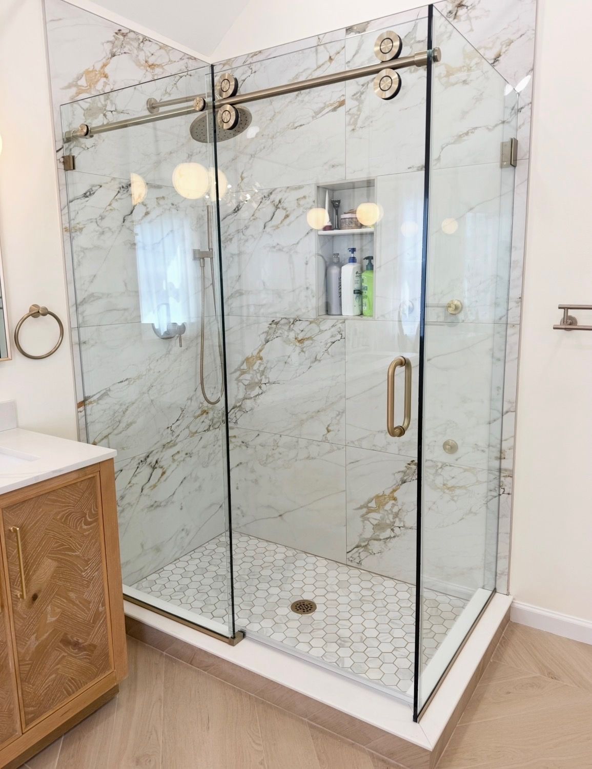 Glass shower enclosure with marble walls and a hex tile floor in a modern bathroom
