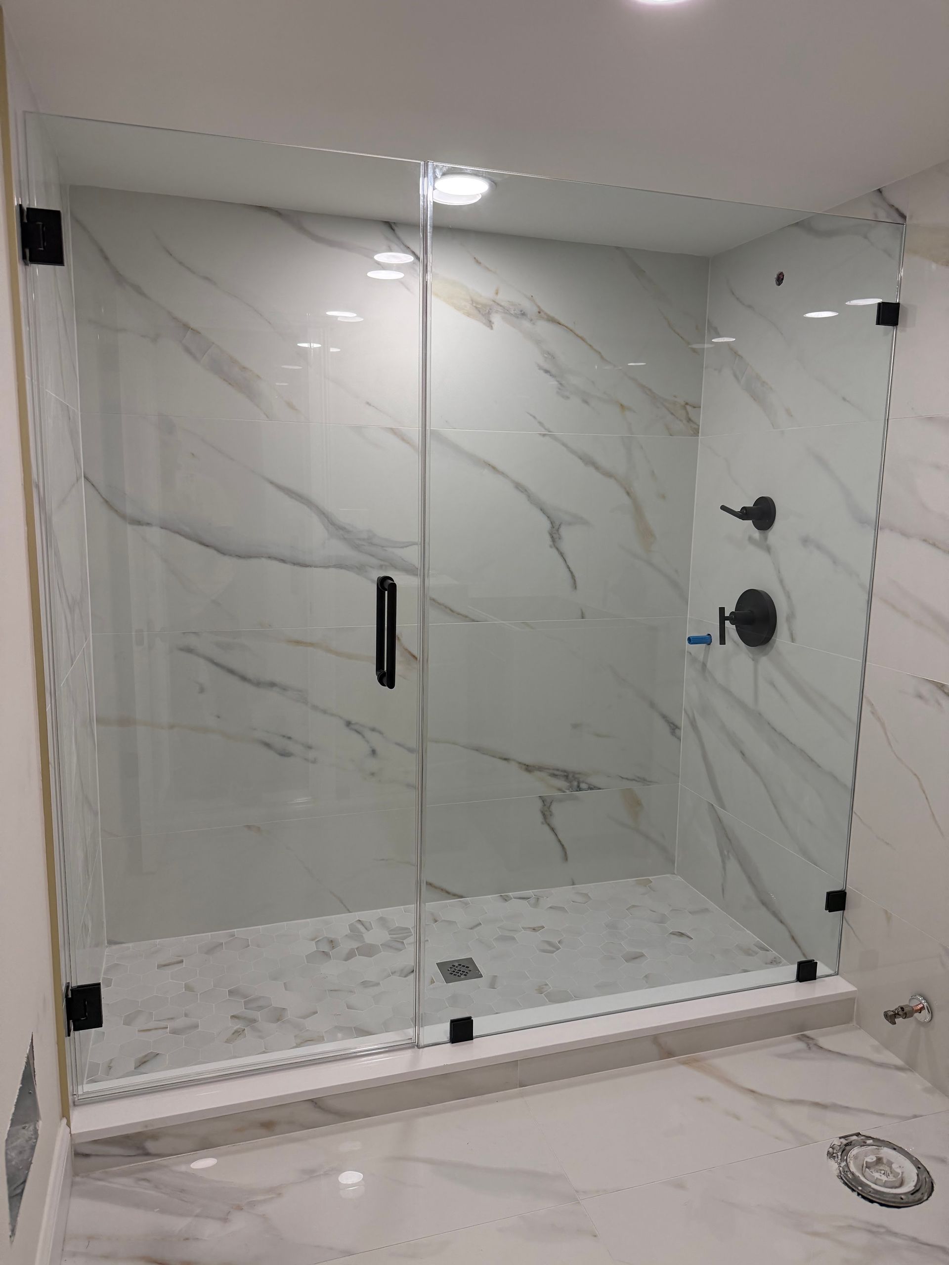Glass shower enclosure with marble-look tile walls and a white tiled floor in a bathroom