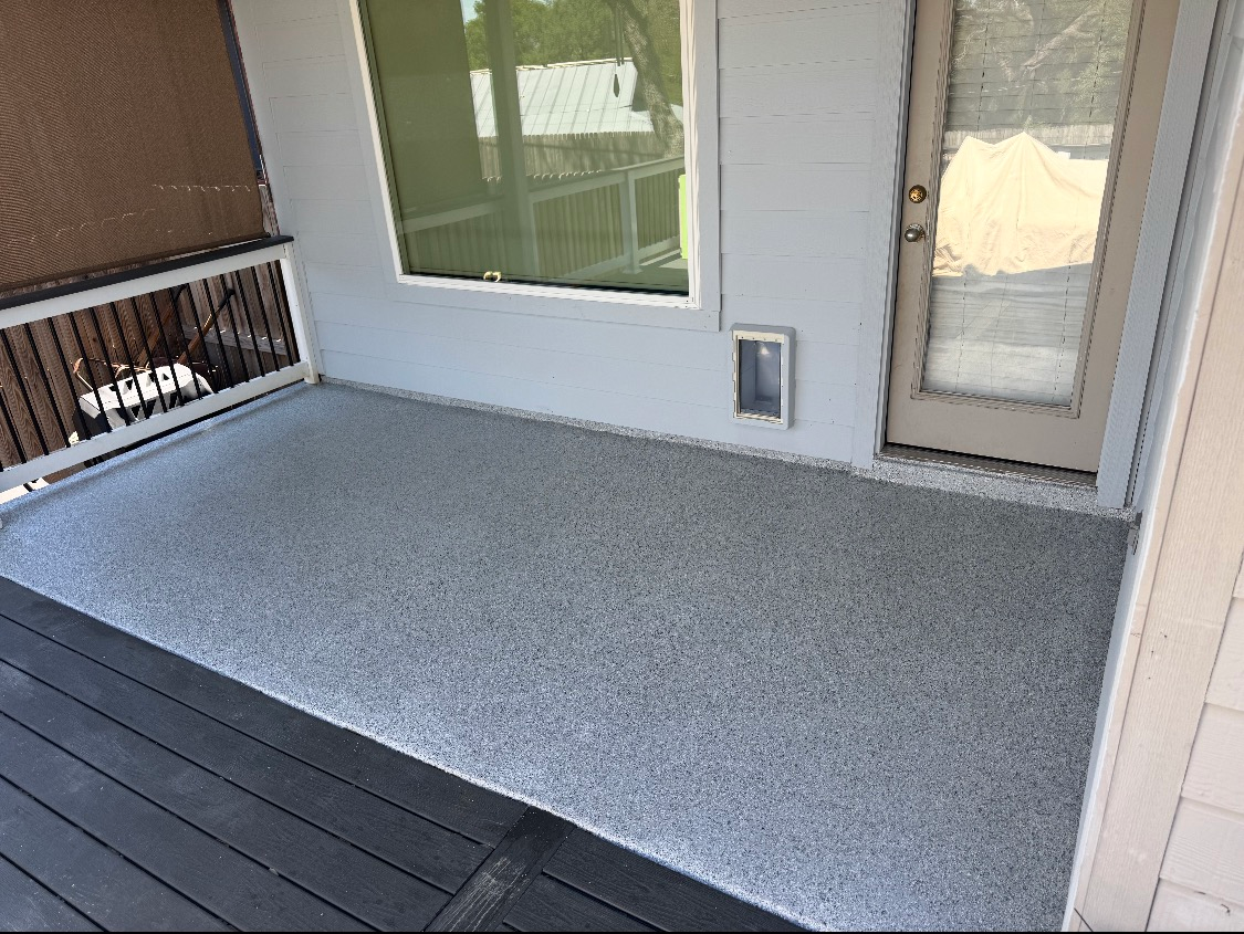 Covered porch with gray speckled concrete floor, dark deck boards, and a screen door beside a window.