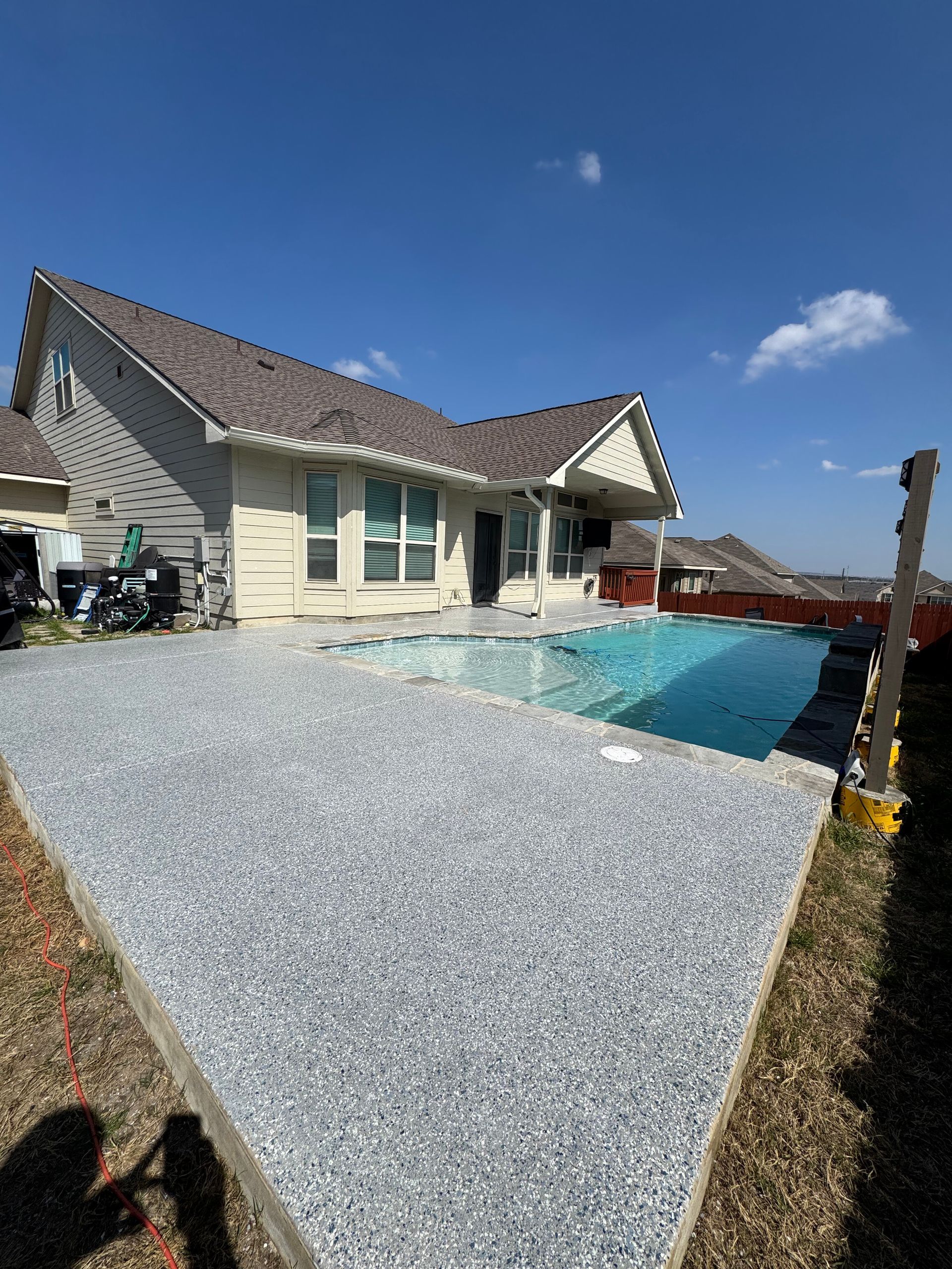 Backyard with a house, gravel patio, and a swimming pool under a blue sky