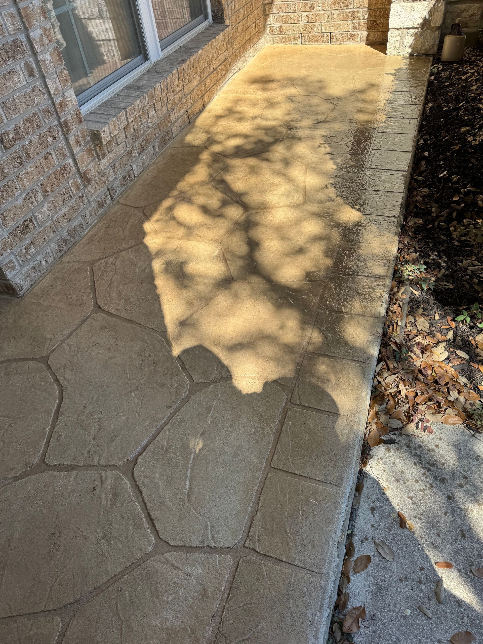 Sunlit brick walkway beside a stone wall, with dappled tree shadows and a narrow gravel edge