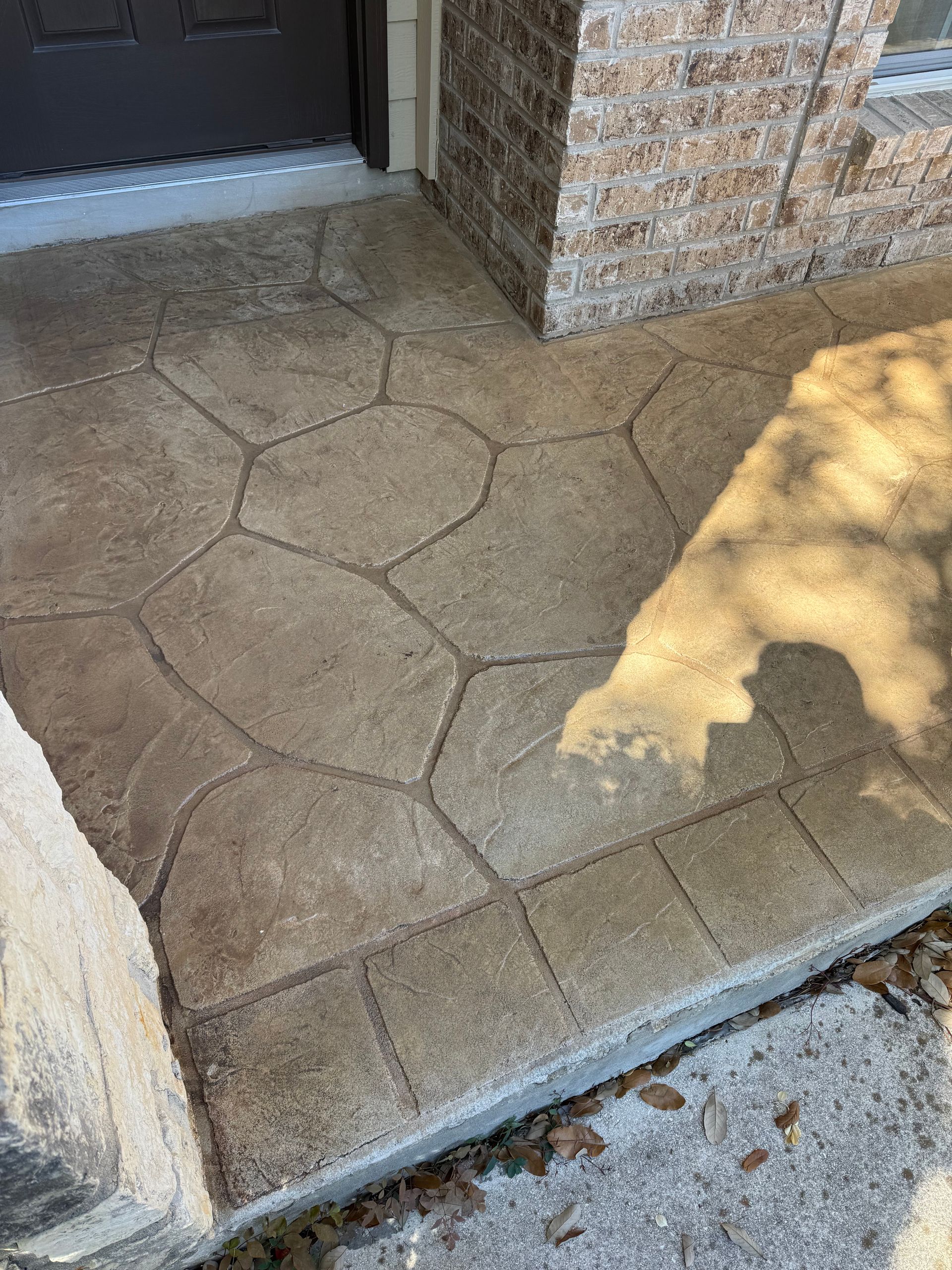 Textured concrete porch with a brick wall, doorway, and a shadow across the ground
