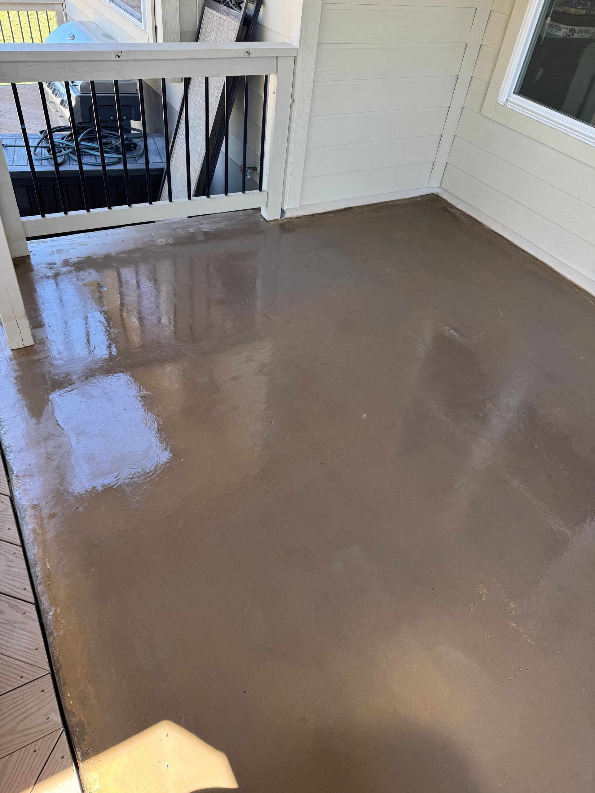 Glossy wet concrete porch with white railing and wall, reflecting light near a doorway