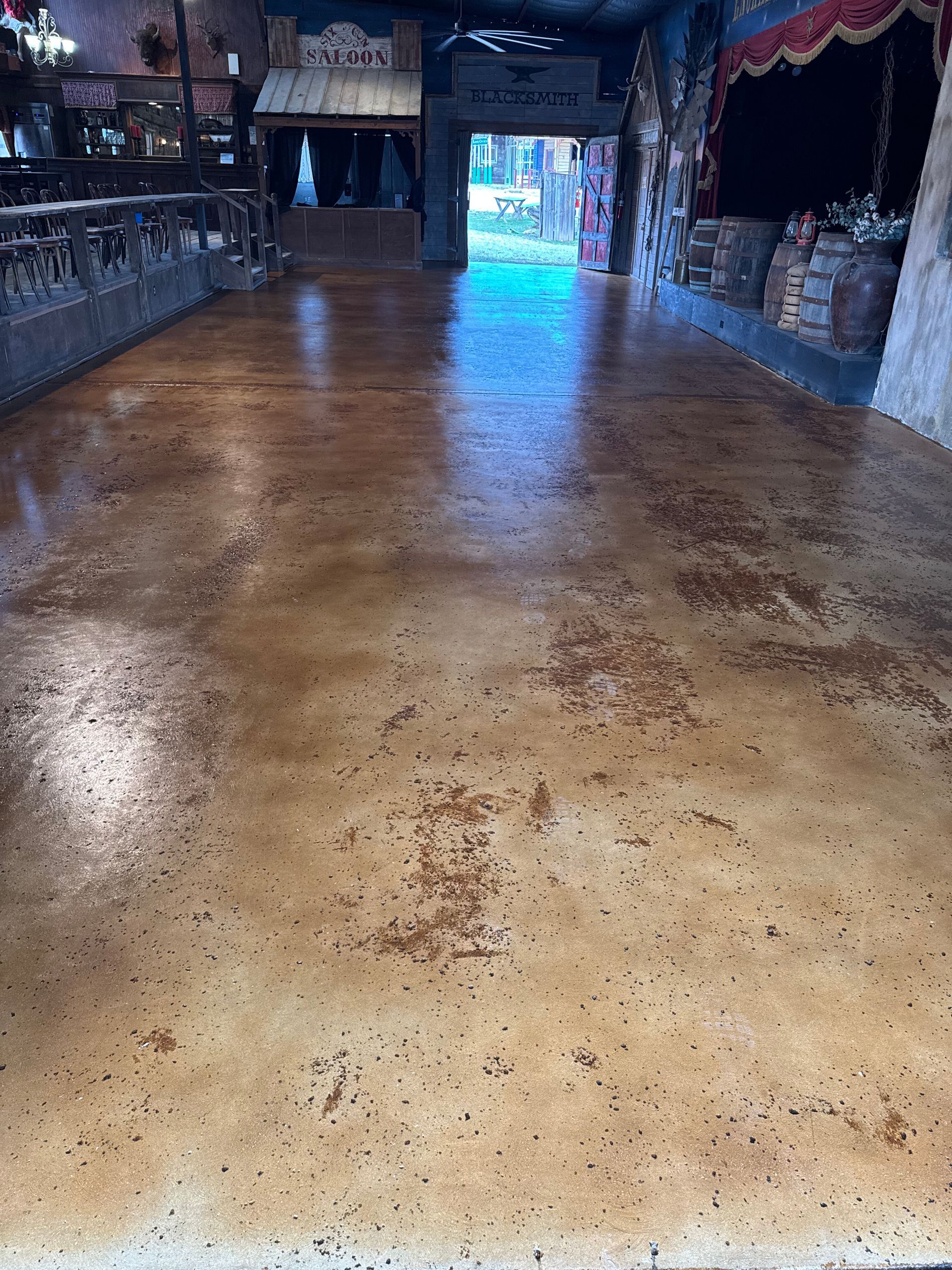 Long polished wooden dance floor in a rustic indoor hall with blue light at the far entrance
