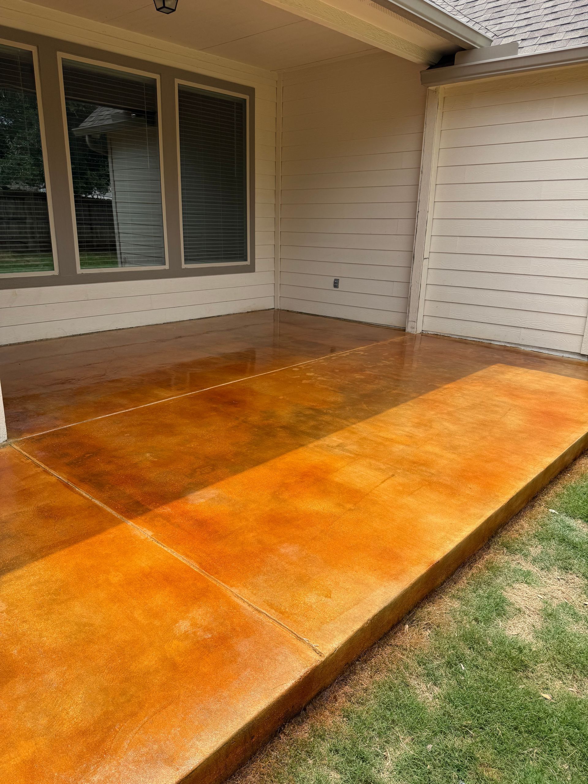 Wooden patio deck beside a house, with windows and white siding in warm sunlight.